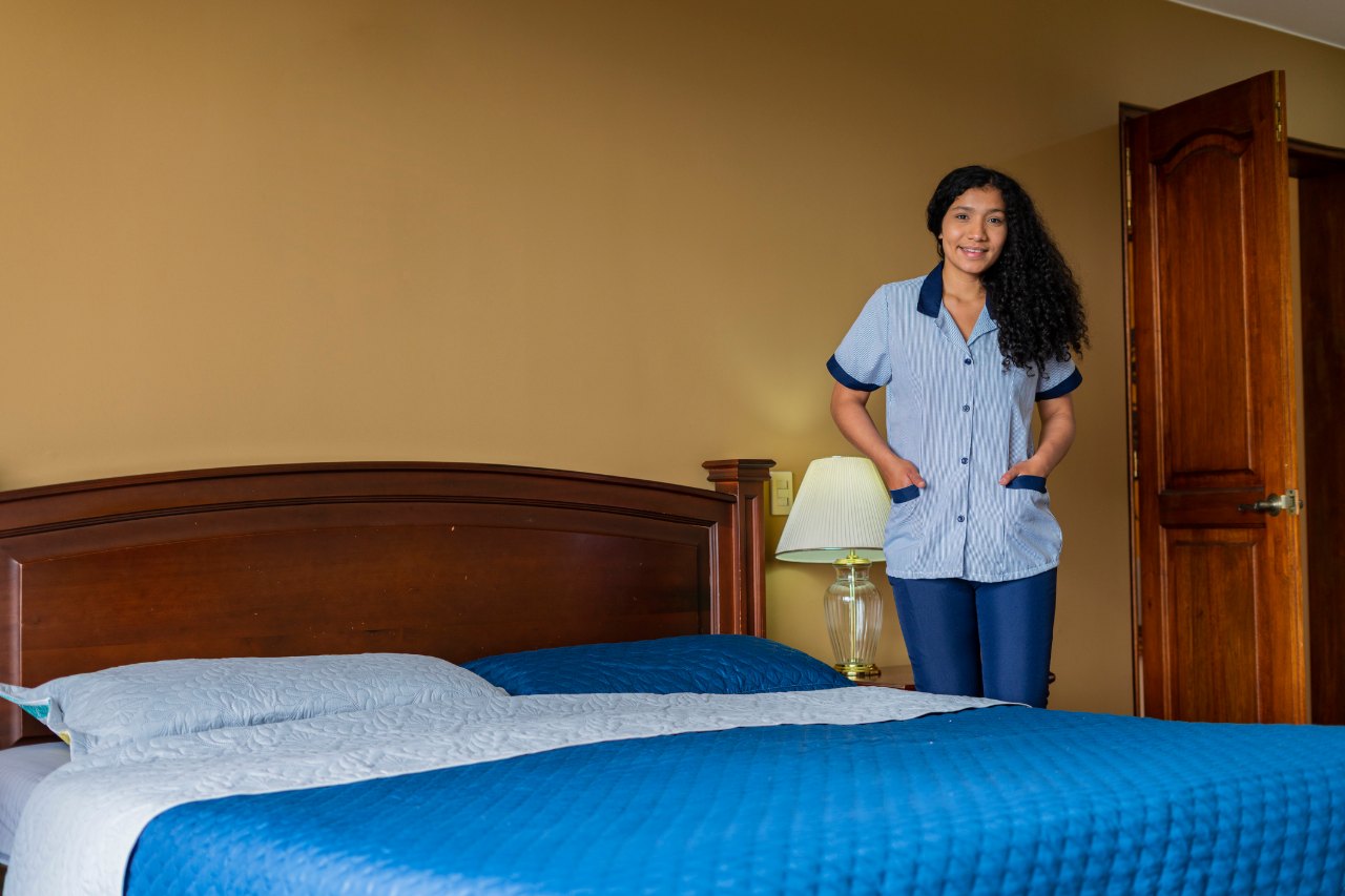 Empleada doméstica con uniforme junto a una cama tendida en una habitación