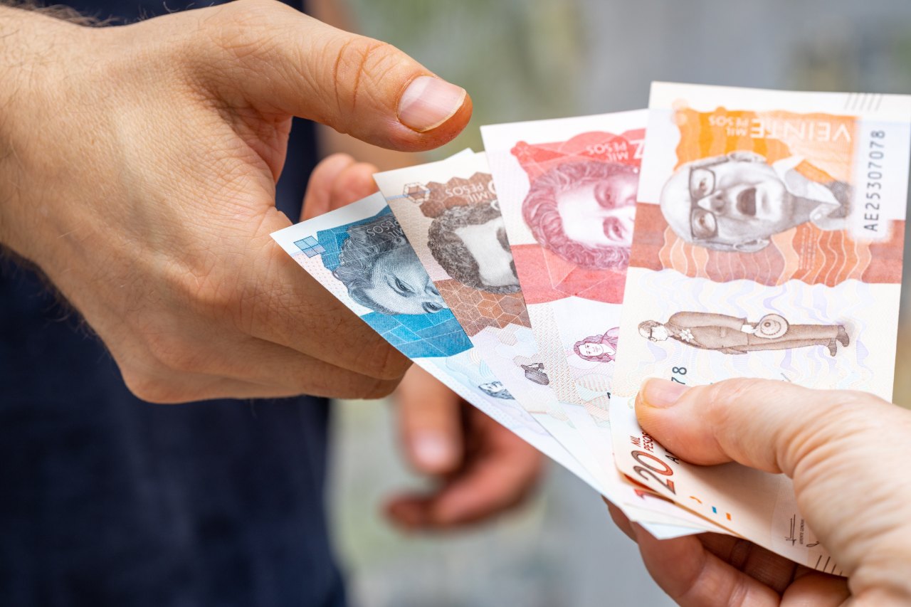 Una mano entrega billetes de pesos colombianos a otra persona